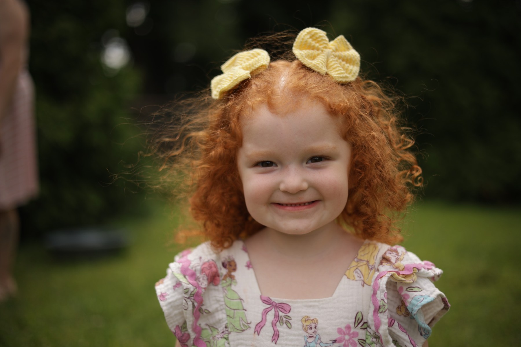 Outdoor portrait of a young child with curly red hair and yellow bows