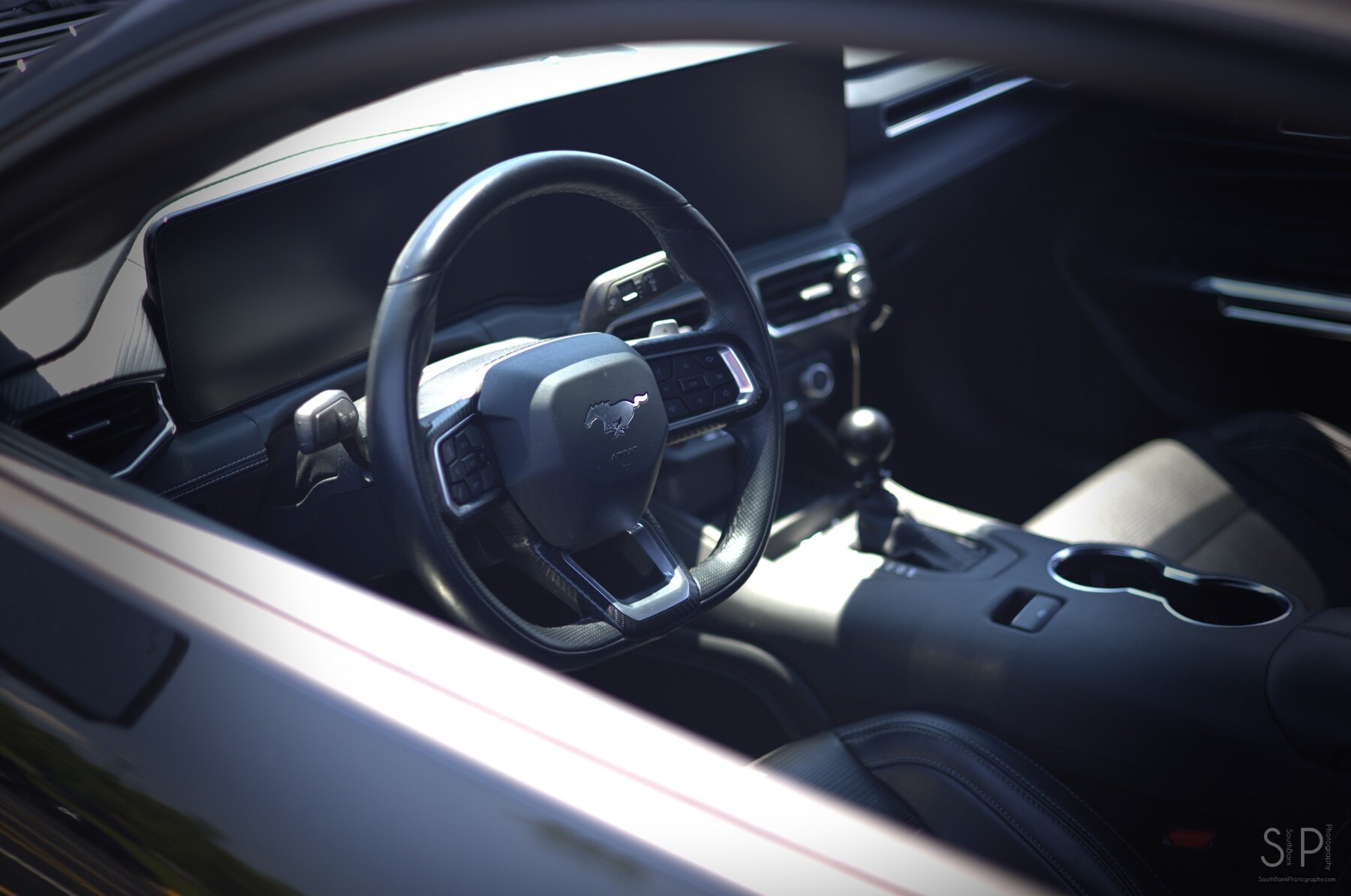 Cool-toned view of the steering wheel and manual shifter inside a modern Ford Mustang