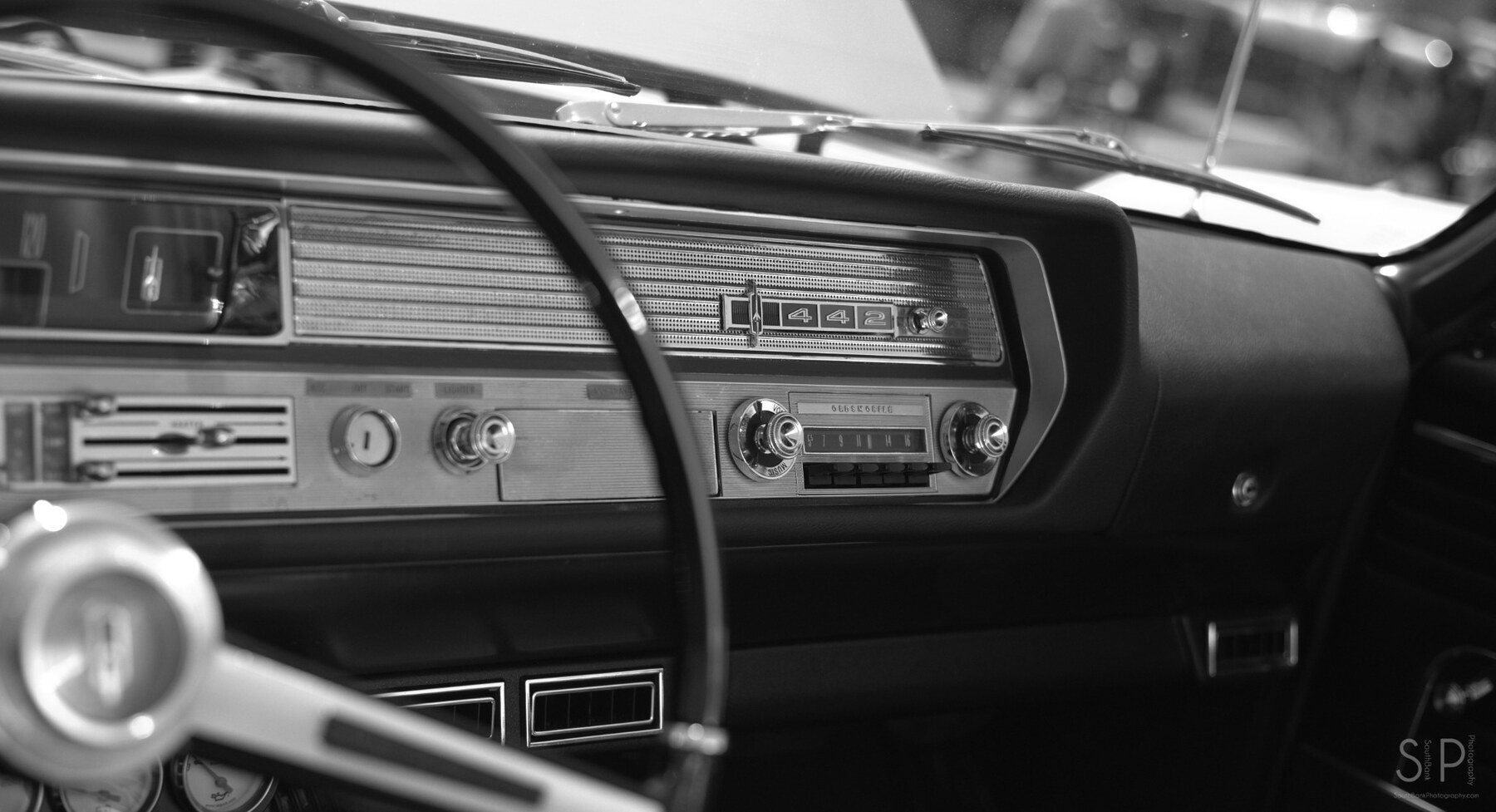 Black and white close-up of the dashboard and 442 emblem inside a 1965 Oldsmobile