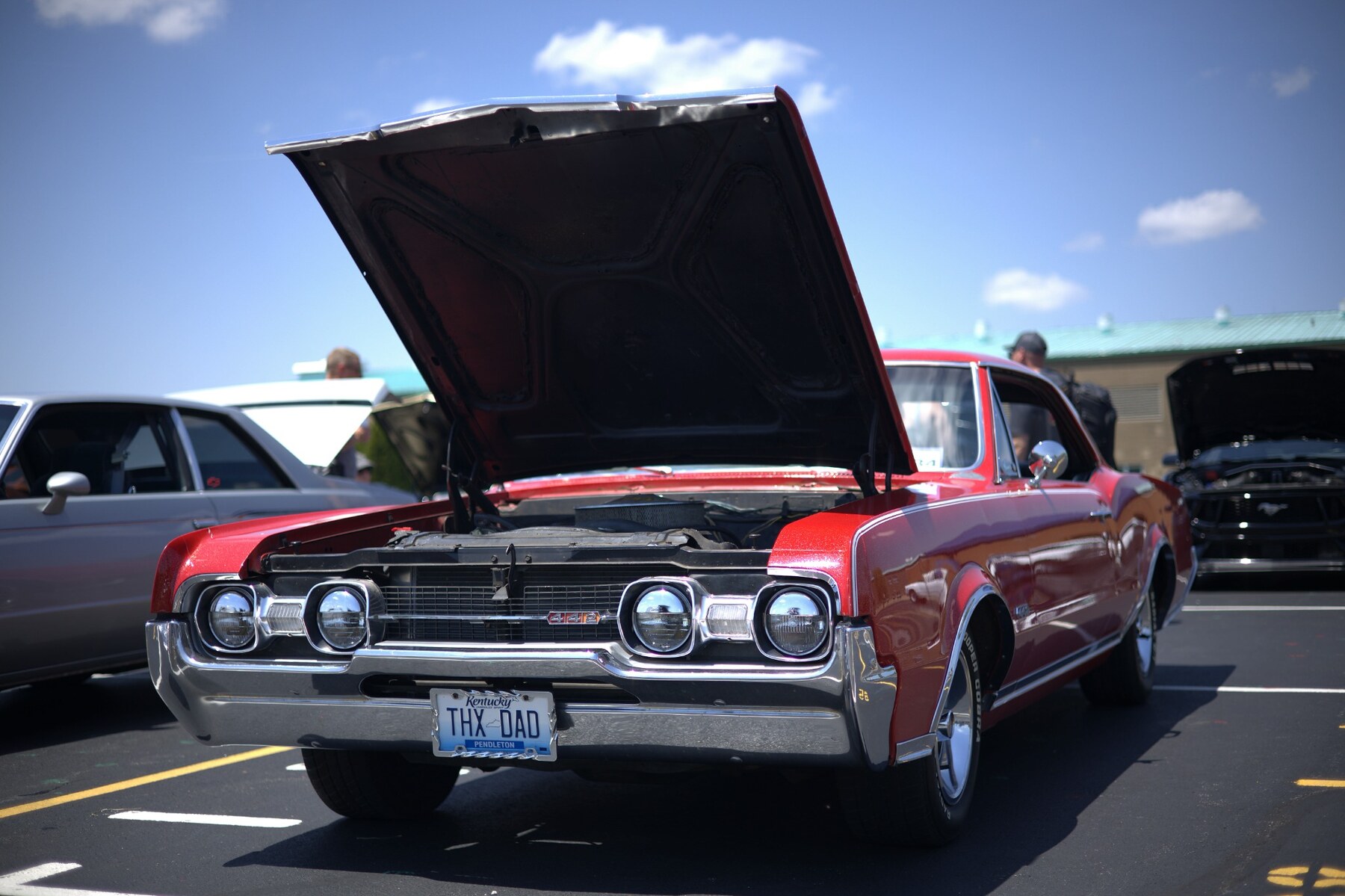 Red classic Oldsmobile 442 displayed with its hood open at a car show