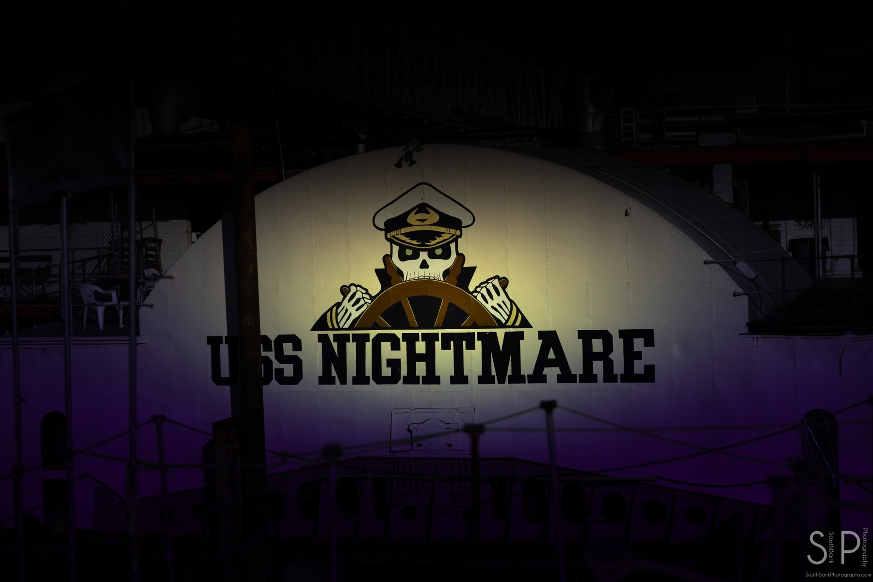 USS Nightmare sign illuminated in a dark industrial riverfront setting